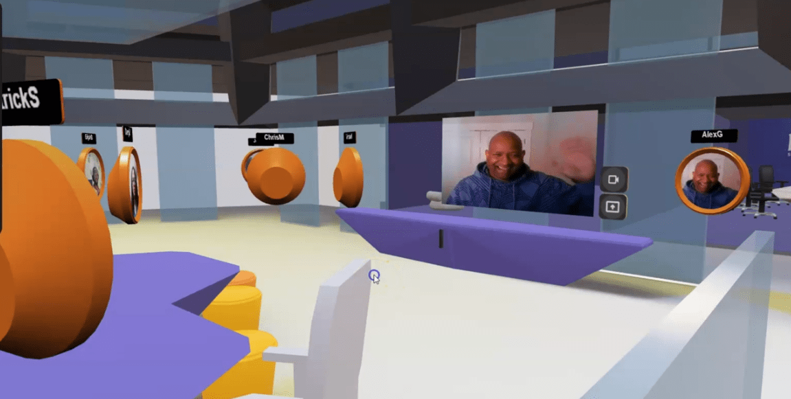 A 3D virtual workspace with a presenter displaying their live work-from-home video for an audience. Each audience member is a circular avatar turned toward the presenter.