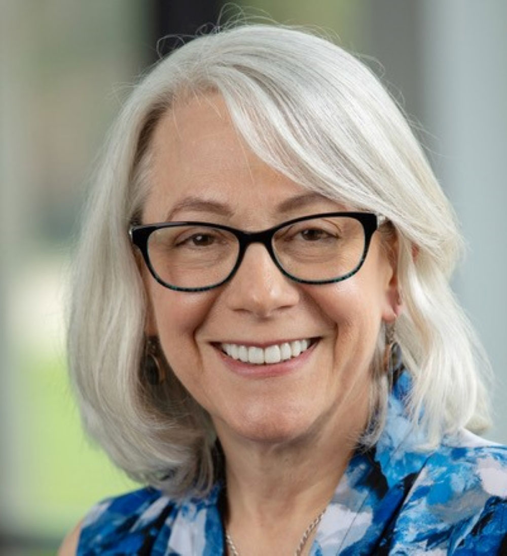 Headshot of Debra Russell with gray mid-length hair and black glasses