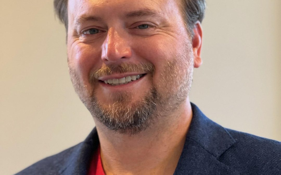 Headshot of Jason Reid - male wearing navy suit with red shirt smiling