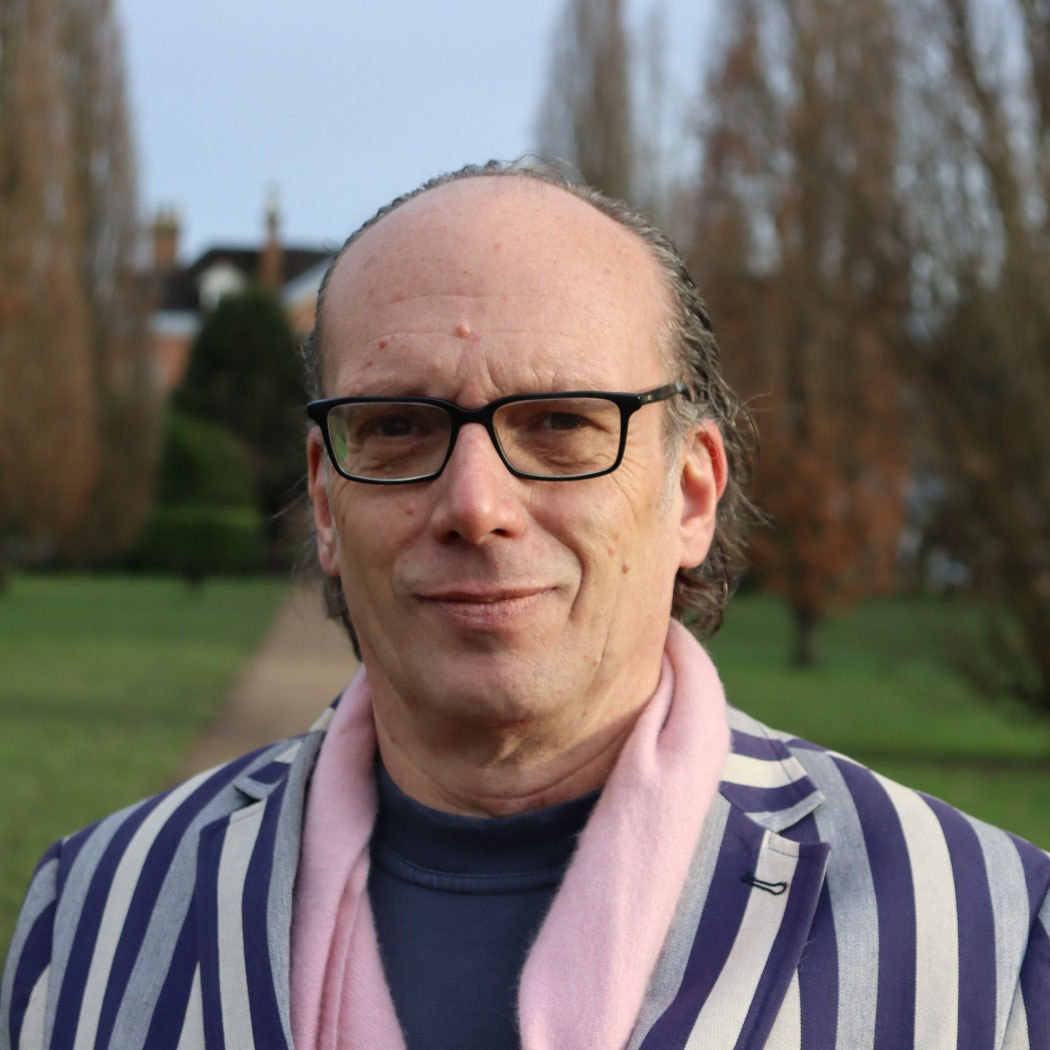 Headshot of Marc Jarret outdoors, wearing glasses and a striped jacket
